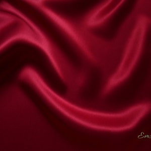 May include: A close-up of a deep red satin fabric with flowing folds and highlights. The fabric has a smooth, lustrous appearance, with shadows adding depth. The word "Emsilk" is in the bottom right corner.