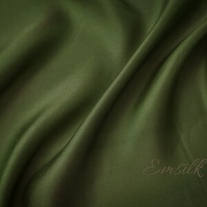 May include: A close-up of a smooth, dark green fabric with a subtle sheen. The fabric is draped in soft folds, creating a luxurious and elegant look. The word "Emsilk" is printed in a brown font on the fabric.