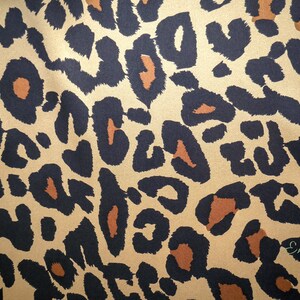 May include: A close-up of a brown and black leopard print fabric. The fabric has a satin-like sheen.