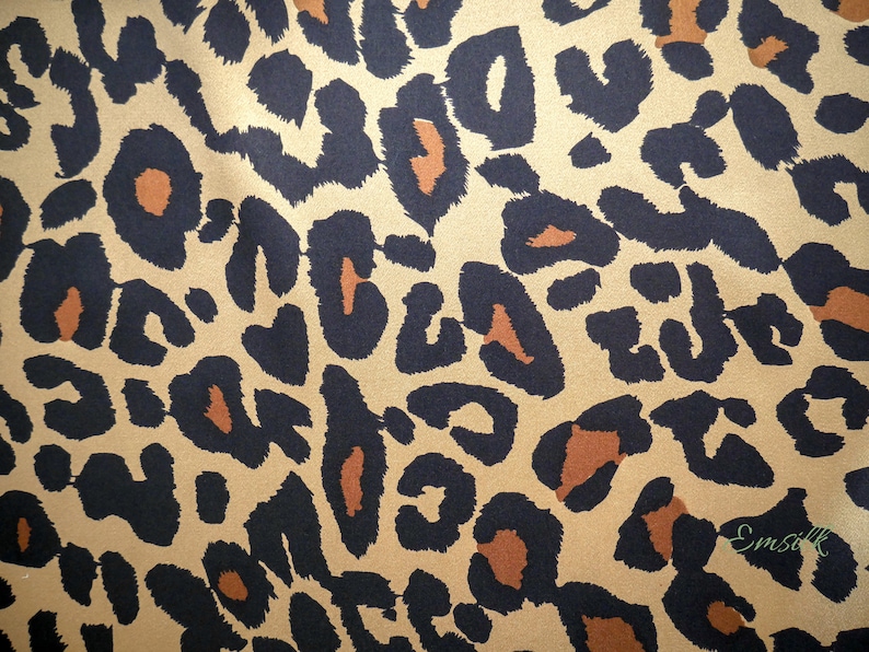 May include: A close-up of a brown and black leopard print fabric. The fabric has a satin-like sheen.