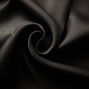 May include: Close-up of a smooth, black fabric with a subtle sheen. The fabric is draped in soft folds, creating a luxurious and elegant look. The text "Emsilk" is visible in the upper left corner.