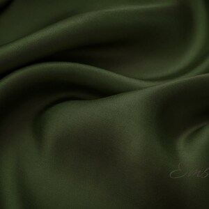 May include: A close-up of a smooth, dark green fabric with a subtle sheen. The fabric is draped in soft folds, creating a luxurious and elegant look.
