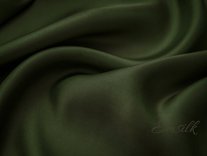 May include: A close-up of a smooth, dark green fabric with a subtle sheen. The fabric is draped in soft folds, creating a luxurious and elegant look.