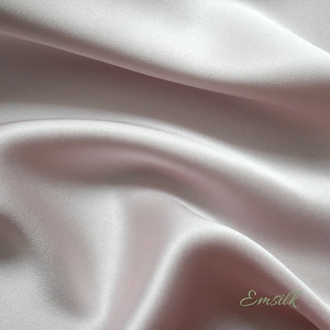 May include: A close-up of a smooth, pale pink satin fabric with a subtle sheen. The fabric is draped and folded, creating soft curves and folds.