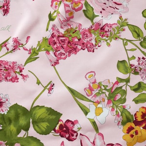 May include: Pink fabric with a floral print featuring various pink, white, and yellow flowers with green leaves. The fabric has the text "Emsilk" printed on it.