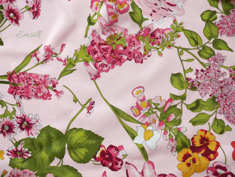 May include: Pink fabric with a floral print featuring various pink, white, and yellow flowers with green leaves. The fabric has the text "Emsilk" printed on it.
