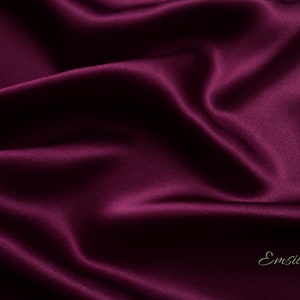 May include: Close-up of a deep purple satin fabric with a subtle sheen. The fabric is smooth and luxurious, with soft folds and wrinkles.