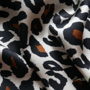 Pode incluir: Close-up de um tecido branco com estampa de leopardo marrom e preto. O tecido é macio e sedoso.