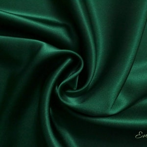 May include: A close-up of a deep green satin fabric, showing its smooth, luxurious texture. The fabric is draped and folded, creating soft curves and folds.