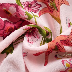 May include: Pink fabric with a floral print featuring lilies and smaller flowers. The fabric has a subtle texture and a soft, flowing drape.