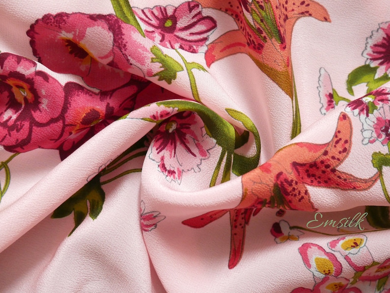 May include: Pink fabric with a floral print featuring lilies and smaller flowers. The fabric has a subtle texture and a soft, flowing drape.
