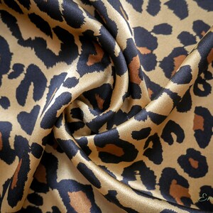 May include: A close-up of a gold and black leopard print fabric. The fabric is made of silk and has a soft, luxurious feel.