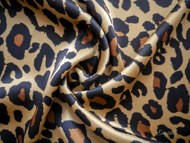 May include: A close-up of a gold and black leopard print fabric. The fabric is made of silk and has a soft, luxurious feel.