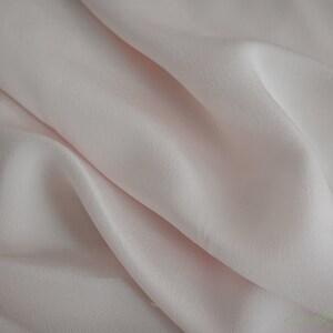 May include: A close-up of a soft, pale pink fabric with a smooth, silky texture. The fabric is draped and folded, creating a gentle, flowing effect.