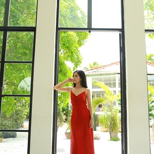 May include: A woman wearing a long, red, sleeveless dress stands in a doorway with a view of a lush green garden.