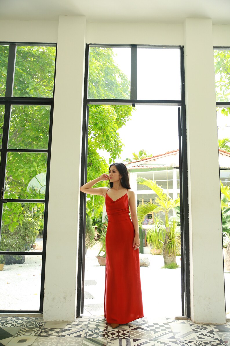 May include: A woman wearing a long, red, sleeveless dress stands in a doorway with a view of a lush green garden.