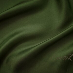 May include: A smooth, dark green fabric with a subtle sheen. The fabric is draped and folded, creating soft curves and folds.