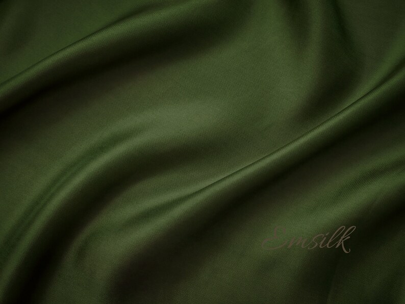 May include: A smooth, dark green fabric with a subtle sheen. The fabric is draped and folded, creating soft curves and folds.