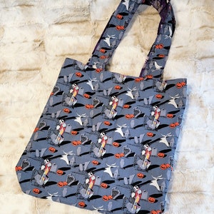 May include: A blue tote bag featuring a repeated pattern of Jack Skellington and Zero from The Nightmare Before Christmas. The design includes pumpkins, tombstones, and a graveyard setting.