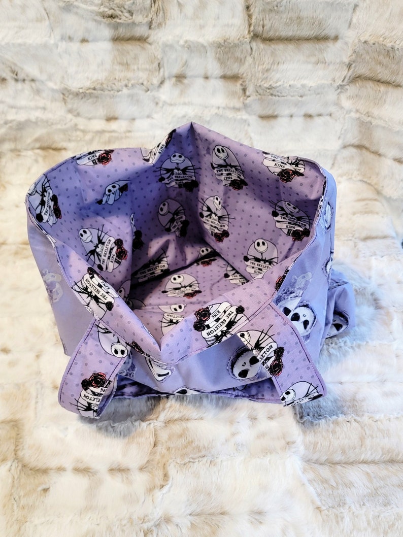 May include: Purple tote bag with a white polka dot pattern and a repeated image of Jack Skellington from The Nightmare Before Christmas. The text "The Skeleton King" is repeated on the bag.