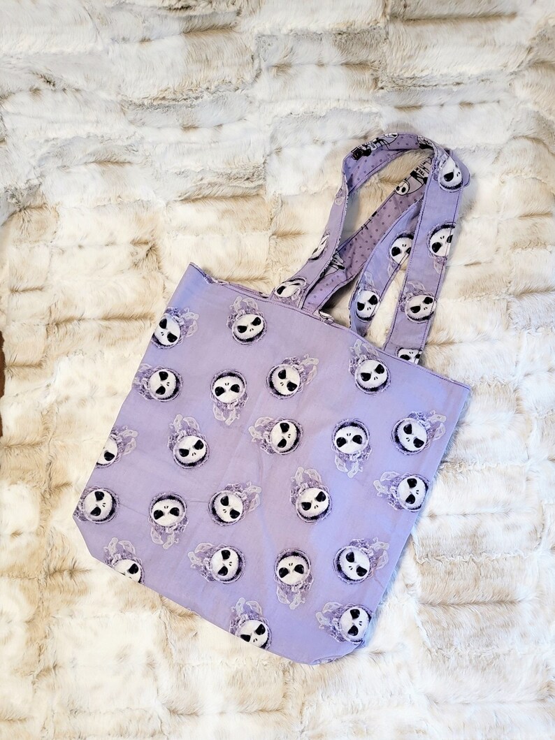 May include: A purple tote bag featuring a repeated pattern of Jack Skellington's face from The Nightmare Before Christmas.