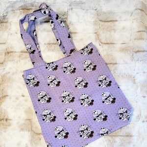 May include: Purple tote bag with a white polka dot pattern and a repeated image of Jack Skellington from The Nightmare Before Christmas. The image includes the text "The Skeleton King".