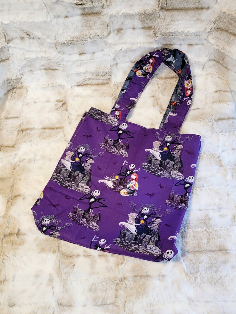 May include: Purple tote bag with a repeating pattern of Jack Skellington and Sally from The Nightmare Before Christmas. The bag has two fabric handles.