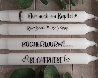 May include: Four white candles with black text and designs. The candles have the following text: "Nur noch ein Kapitel", "Read Books - Be Happy", "BÜCHERWURM", and "BÜCHERLIEBE".