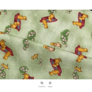 May include: Pale green fabric featuring a repeating pattern of yellow ducklings on red sleds, small white flowers, and green patches. The fabric is folded, showing the texture and design.