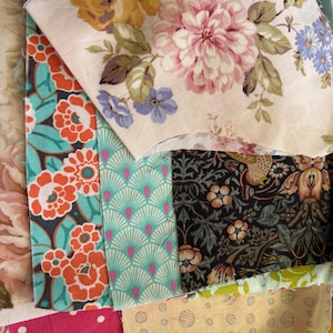 May include: A collection of fabric scraps in various patterns and colours, including floral, geometric, and polka dot designs. The fabrics are arranged in a patchwork style, with some pieces overlapping.