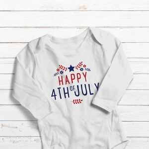 May include: White long-sleeve baby onesie with red and blue text that reads "Happy 4th of July" with a star and floral accents.