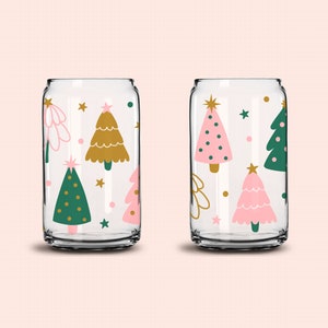 May include: Two clear glass tumblers with a Christmas tree pattern. One tumbler has pink, green, and gold trees. The other tumbler has gold, green, and white trees.