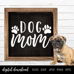 以下が含まれることがあります： 「DOG mom」と白文字で書かれた黒い看板。看板の「DOG」の両側に肉球の跡がある。看板の前に、茶色と白の小さな子犬が座っている。