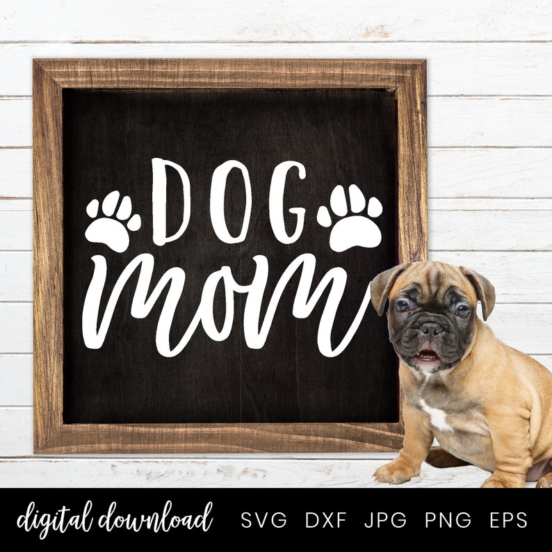 以下が含まれることがあります： 「DOG mom」と白文字で書かれた黒い看板。看板の「DOG」の両側に肉球の跡がある。看板の前に、茶色と白の小さな子犬が座っている。