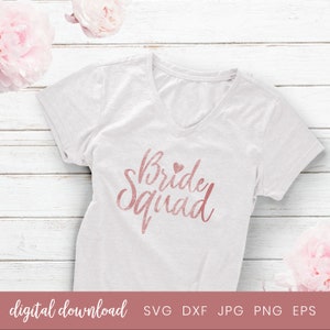 May include: A white t-shirt with a rose gold graphic that says "Bride Squad" with a small heart above the word "Bride".