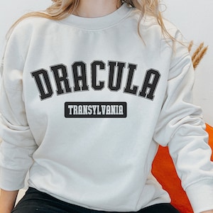 Op de afbeelding: Een cr&egrave;mekleurig sweatshirt met zwarte tekst die "Dracula Transsylvani&euml;" zegt.