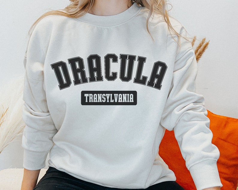 Op de afbeelding: Een cr&egrave;mekleurig sweatshirt met zwarte tekst die "Dracula Transsylvani&euml;" zegt.