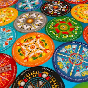 May include: A set of colorful round tarot cards with intricate mandala designs. Each card features a different symbol and text, including "The Fool", "Queen of Swords", "Justice", and "8 of Cups".