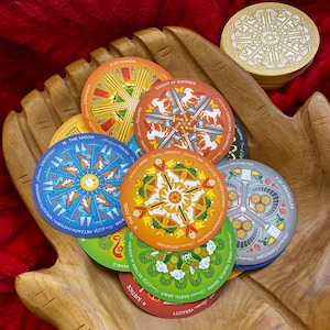 May include: A set of colorful tarot cards with mandala designs. The cards feature various symbols and imagery, including the moon, a knight, a fool, and wands. The cards are arranged in a circle on a wooden surface.