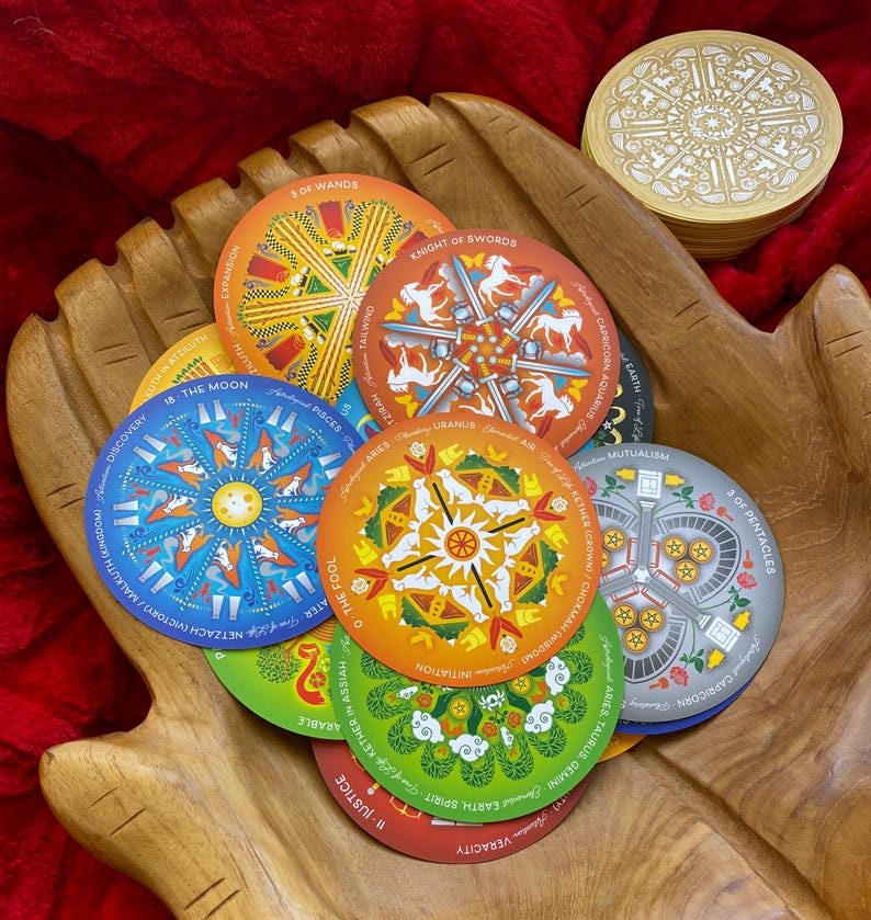 May include: A set of colorful tarot cards with mandala designs. The cards feature various symbols and imagery, including the moon, a knight, a fool, and wands. The cards are arranged in a circle on a wooden surface.