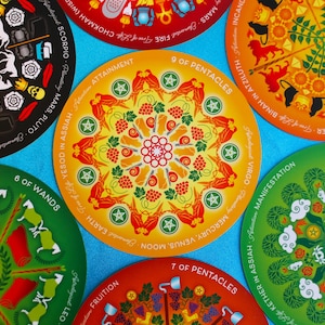May include: Nine tarot cards with colorful mandala designs. Each card features a different astrological sign and a number. The cards are arranged in a circle on a blue background.