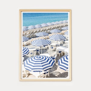 Puede incluir: Una escena de playa con sombrillas a rayas azules y blancas y sillas blancas en una playa de guijarros. Las sombrillas est&aacute;n dispuestas en filas y hay un mar azul claro en el fondo.