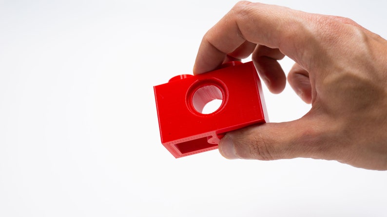 May include: A red plastic building block with a hole in the center. The block has a smooth surface and is designed for connecting with other blocks.