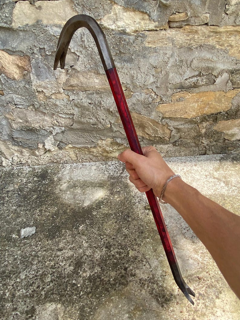 May include: A metal crowbar with a curved end and a forked tip. The handle is a deep red color. The tool is designed for prying and demolition.