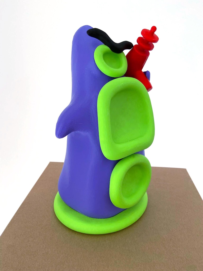 May include: A whimsical, abstract sculpture in shades of purple and green, with a red element. The sculpture has a rounded form with circular and rectangular green accents. A black, curved shape and a red object are attached to the top.