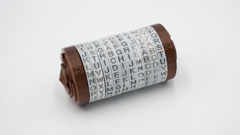 May include: A brown metal cylinder with multiple rotating discs, each with the alphabet printed on it. The cylinder is a letter-based cipher device.