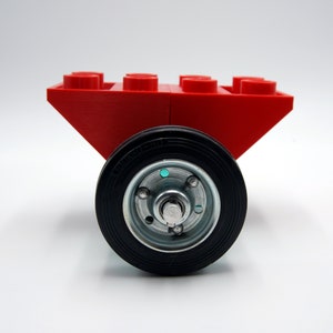 Puede incluir: Un carro de juguete rojo con cuatro ruedas. El carro est&aacute; hecho de bloques de construcci&oacute;n de pl&aacute;stico y tiene una rueda de goma negra con un cubo plateado.