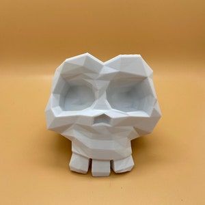 Op de afbeelding: Witte, geometrisch ontworpen schedel plantenpot. De schedel heeft een uitgeholde oogkas en een kleine, open mond.