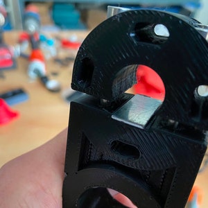 May include: Close-up of a black 3D printed object with a silver metal piece inserted into it. The object has a textured surface and a circular opening.