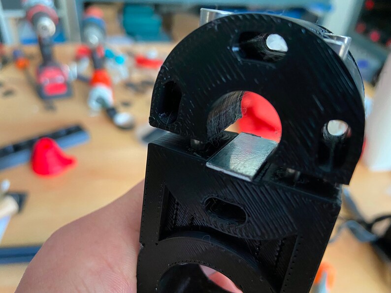 May include: Close-up of a black 3D printed object with a silver metal piece inserted into it. The object has a textured surface and a circular opening.